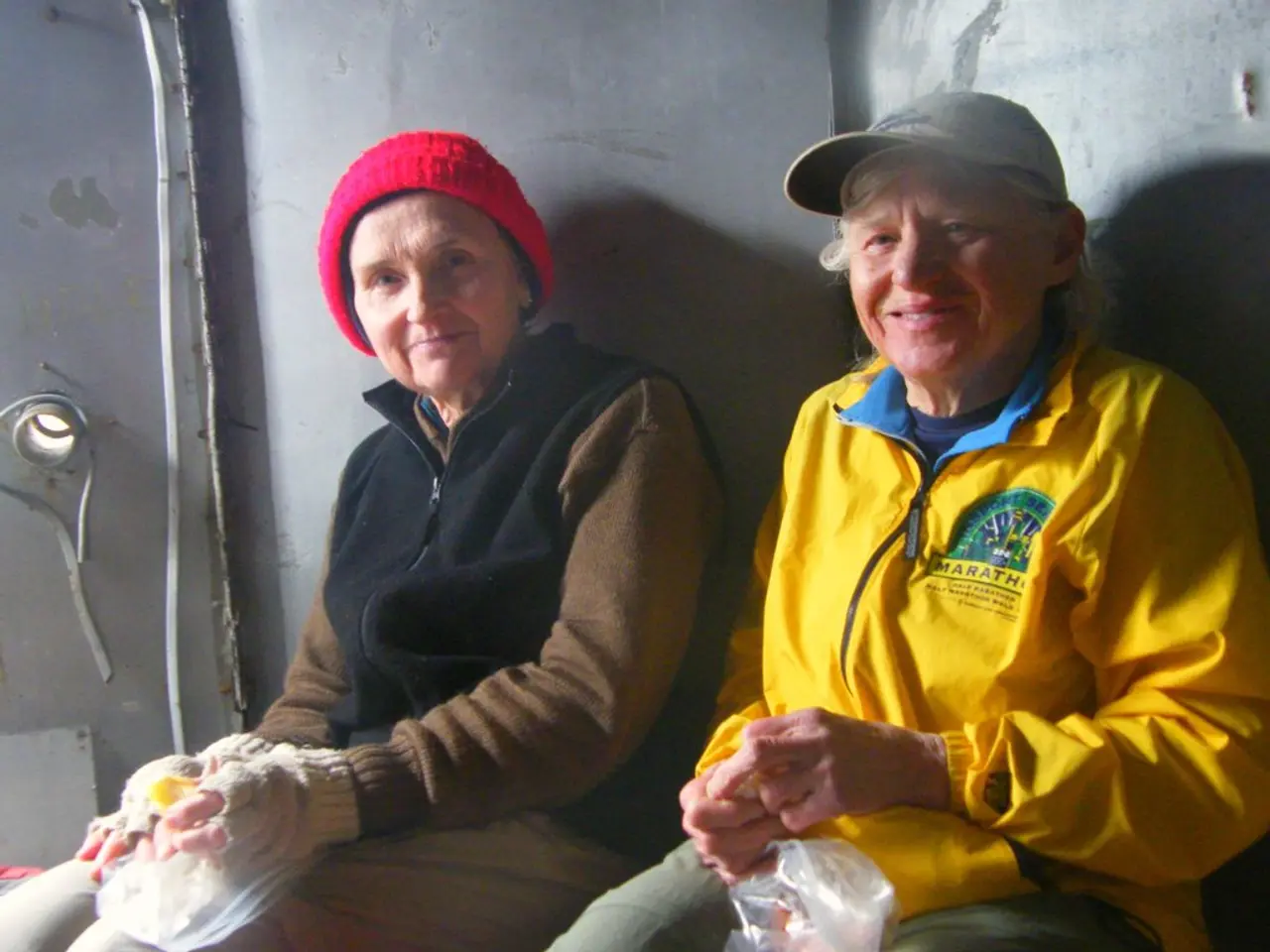 Here in this picture we can see two old women, wearing jackets and caps sitting over a place and we...
