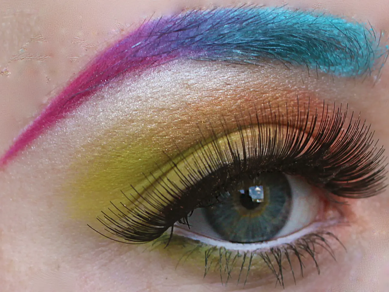 This picture shows a human eye with color painting to it and we see color to the eyebrow and color...