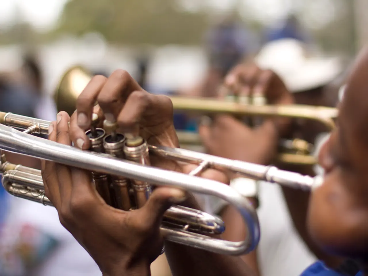 In this picture we can see two persons playing trumpets, we can see a blurry background here.