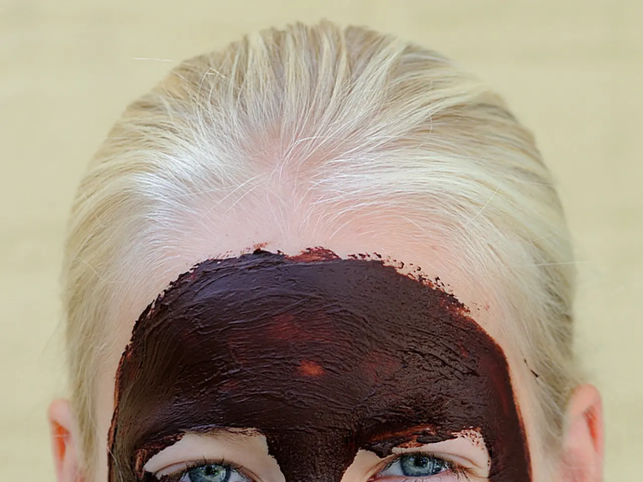 In this image I see a person who is smiling and I see the face mask on the face which is of brown...