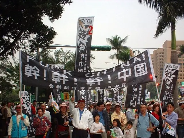 In the image there are many women and men standing on the road holding banners and flags, they...