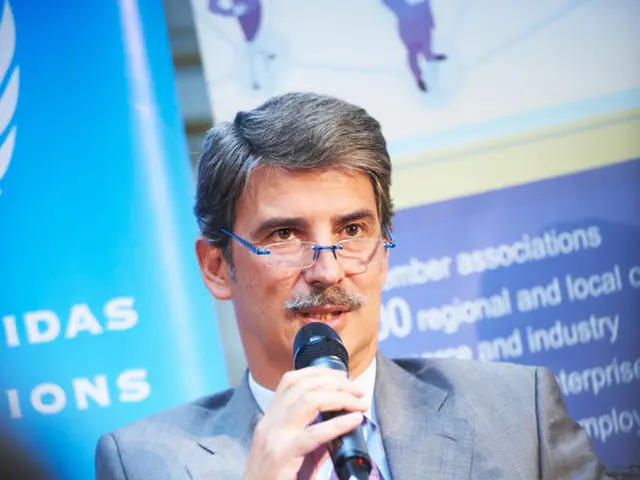 This person is sitting on a chair, holds file and talking in-front of mic. Backside of this person...