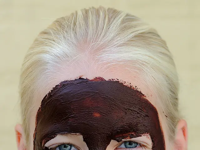 In this image I see a person who is smiling and I see the face mask on the face which is of brown...